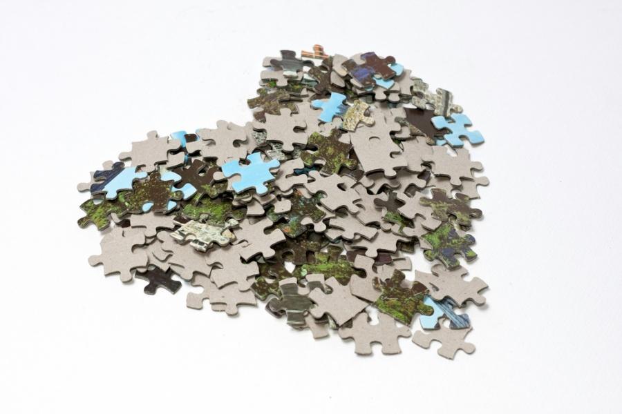 A+pile+with+lots+of+small+jigsaw+puzzle+pieces+having+a+gray+back+and+a+front+picture+made+of+cyan+and+green+colors.+They+are+arranged+in+the+shape+of+a+heart%2C+on+a+white+background.
